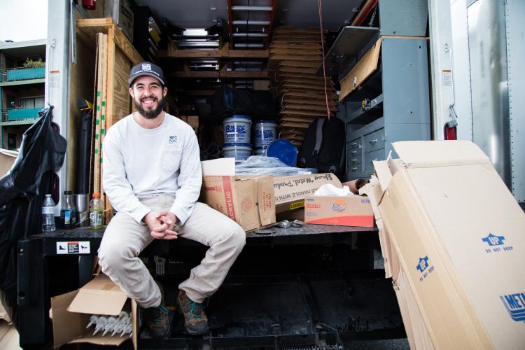 A weatherization worker smiles sitting in the back of a boxtruck. 