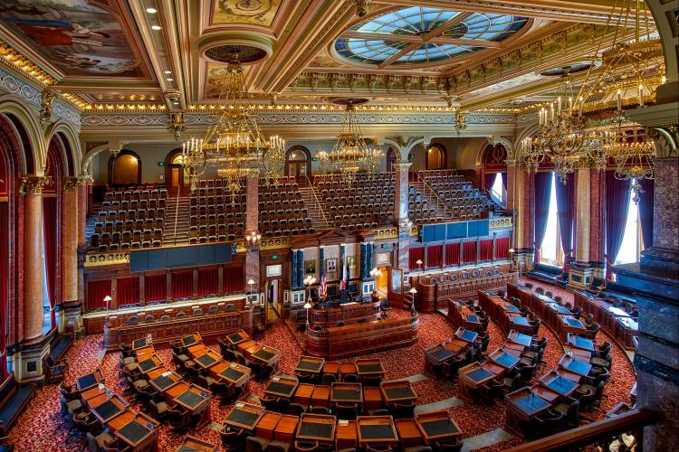 Interior of the Iowa state legislature - desks and dark wood with a gilded ceiling