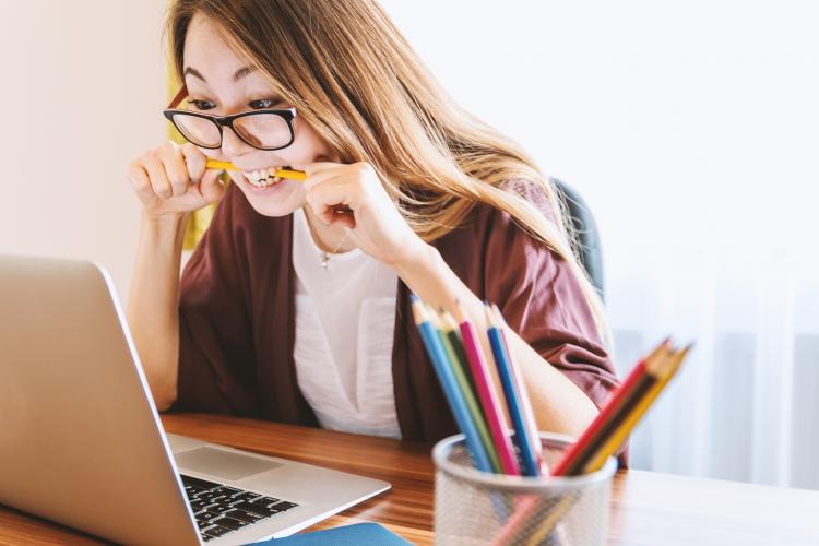 woman biting pencil while sitting on chair in front of computer